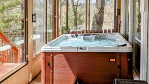 A hot tub in a wooden cabin with a glass door, a wooden deck, and a view of trees.