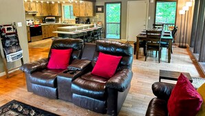 A spacious living area with a leather sofa, a dining table, and a kitchen in the background.