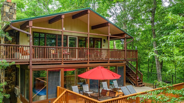 A two-story cabin with a balcony, outdoor seating area, and a stone chimney.
