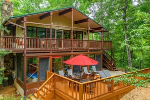 A two-story cabin with a balcony, outdoor seating area, and a stone chimney.