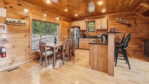 A wooden cabin interior with a dining area, kitchen, and a sign indicating a pool direction.