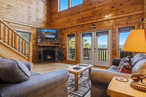 A log cabin interior with a fireplace, a television, a sofa, and a view of the outdoors. - Private Pool*Theater Room*Game Room W/ Pool Table*WiFi/Cable (SEVIERVILLE)