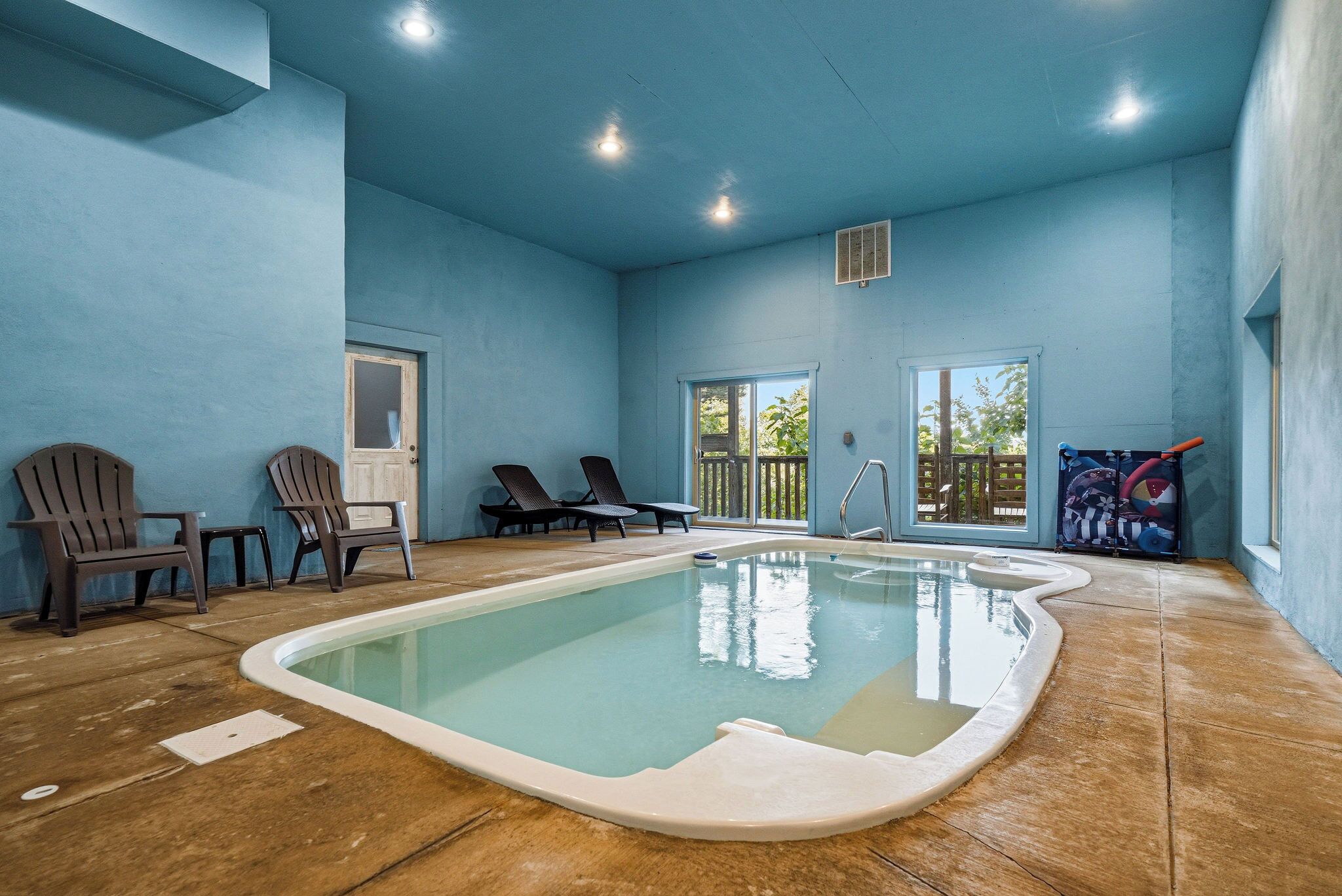 A swimming pool with a tiled floor, two lounge chairs, and a door.