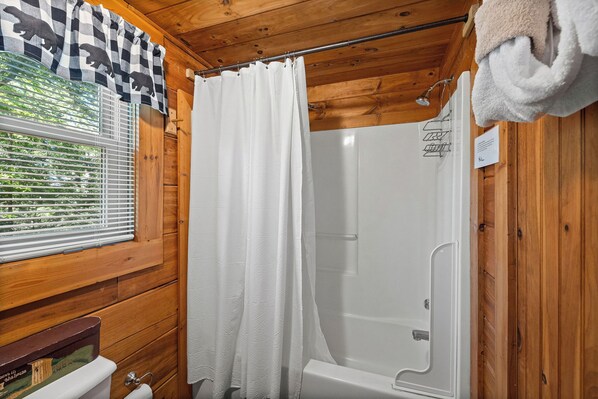 A wooden cabin bathroom with a shower, a toilet, and a window with blinds.