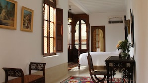 A room with a bed, a chair, a table with a vase, and a patterned rug. - El Morocco Hotel (Marrakech)
