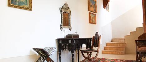 A room with a patterned carpet, a wooden chair, a small table, and a staircase.