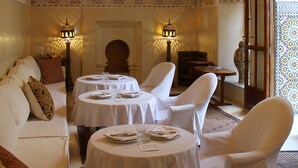A traditional interior with ornate patterns, a chandelier, and a seating area with tables set for dining. - El Morocco Hotel (Marrakech)