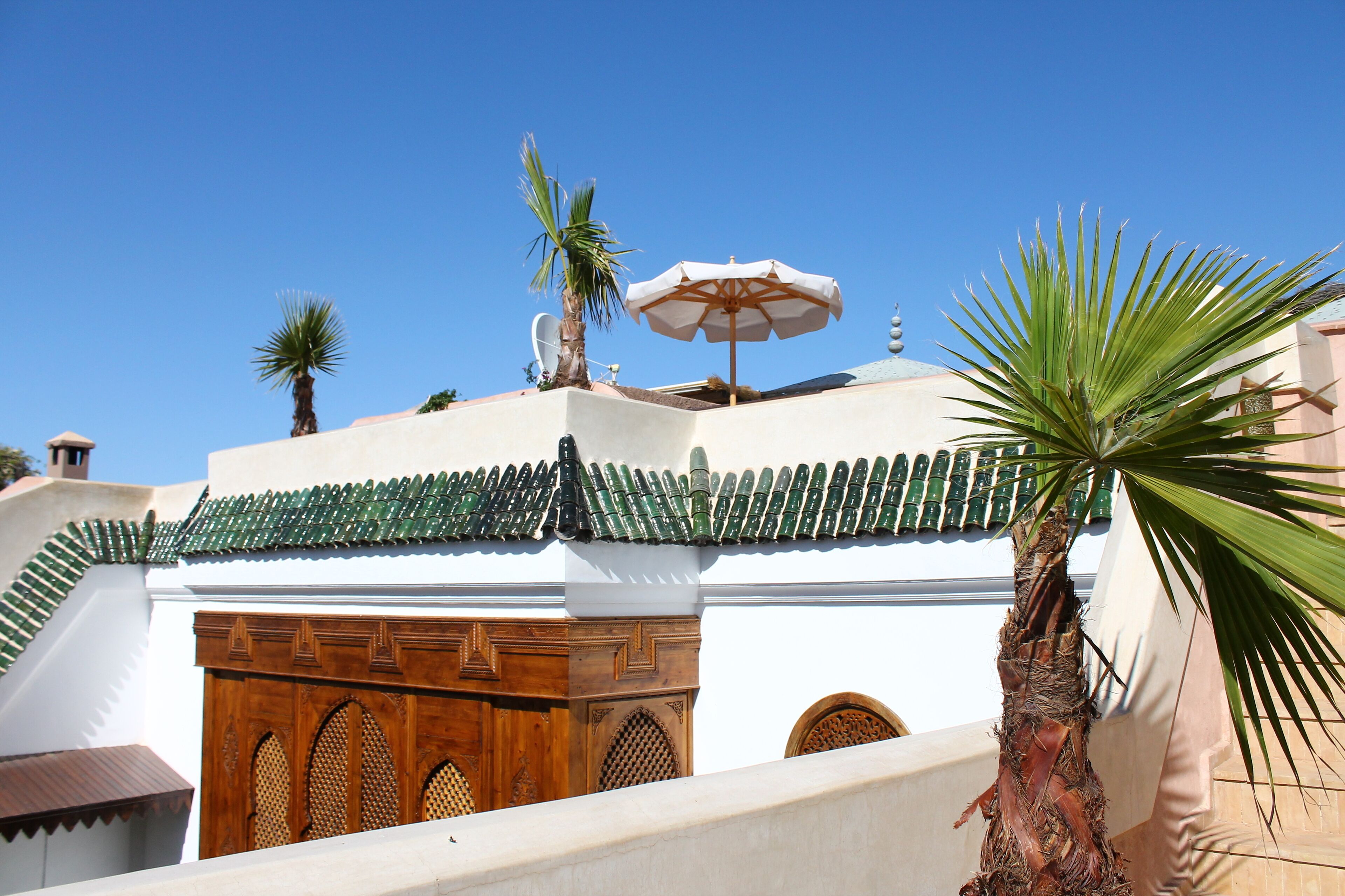 Un edificio con tejado de tejas verdes, una puerta de madera con intrincados grabados y una palmera en primer plano.