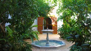 A courtyard with a fountain, surrounded by lush greenery and a building with ornate doors. - El Morocco Hotel (Marrakech)