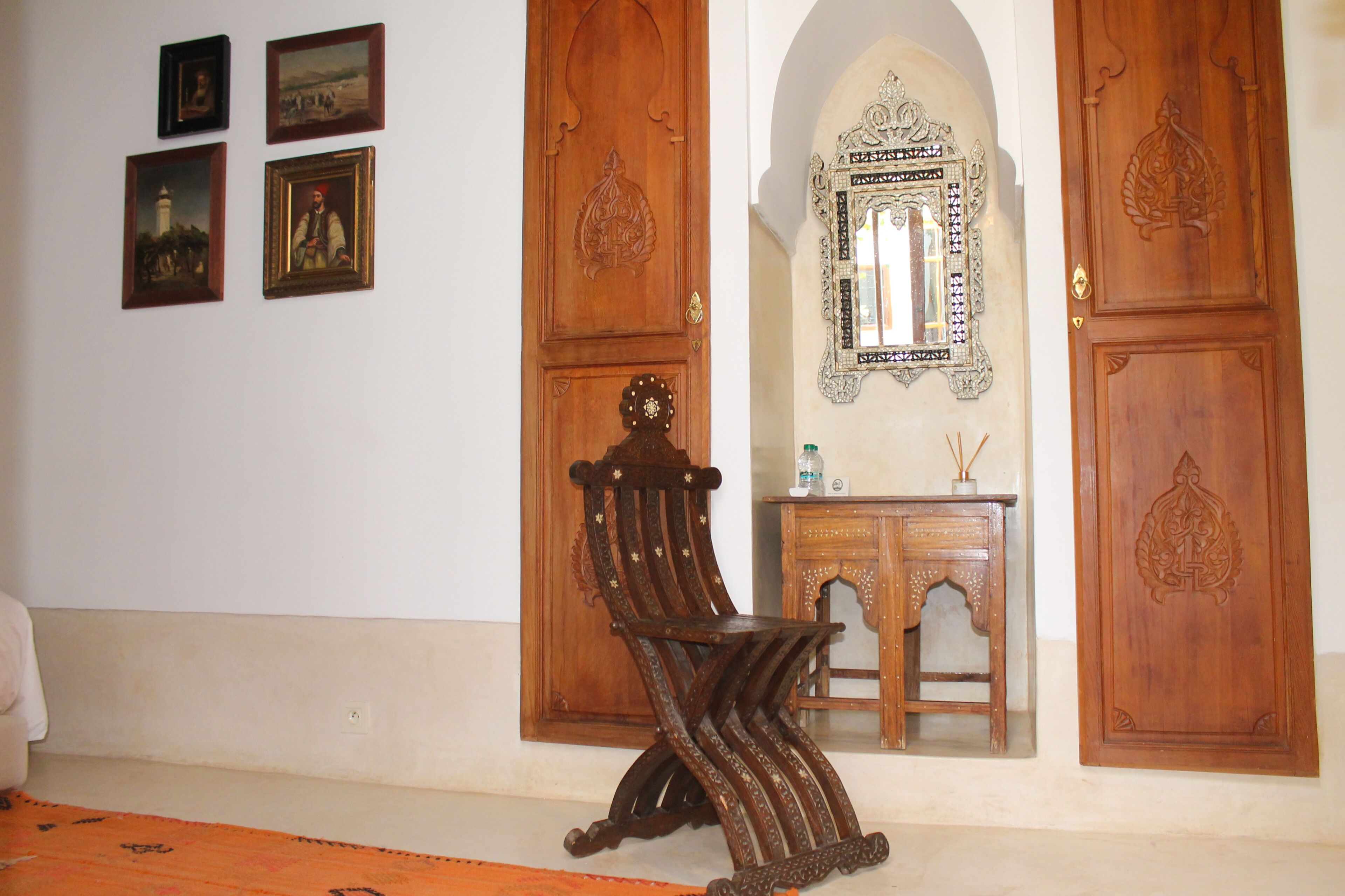 Una habitación con una silla de madera, una mesita y un espejo en la pared.