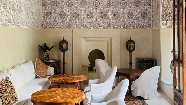 A room with a high ceiling, intricate wall patterns, a chandelier, white furniture, and traditional decor. - El Morocco Hotel (Marrakech)