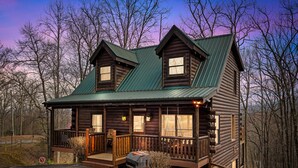 Une cabane en rondins avec un porche, un barbecue et une vue sur la forêt environnante.