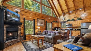 L’intérieur d’une cabane en rondins, avec une cheminée en pierre, des meubles en bois, un coin repas et une cuisine.
