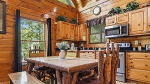 L’intérieur d’un chalet en bois comprend une table à manger, des chaises, une cuisine équipée et une fenêtre avec des rideaux.