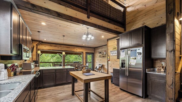A modern kitchen with wooden beams, a central island, stainless steel appliances, and a large window offering a view of greenery. - Gatlinburg*Resort*Breathtaking Views*Keurig*Wifi*Hot Tub (GATLINBURG)