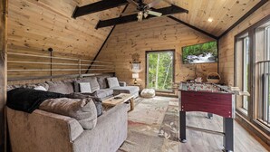 A cozy room with a wooden ceiling, a sofa, a foosball table, and a TV screen displaying a nature scene. - Gatlinburg*Resort*Breathtaking Views*Keurig*Wifi*Hot Tub (GATLINBURG)