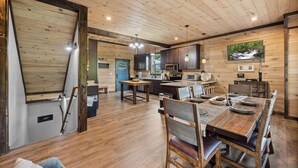 A spacious kitchen with wooden cabinets, a dining area with a large wooden table, and a TV mounted on the wall displaying a forest scene. - Gatlinburg*Resort*Breathtaking Views*Keurig*Wifi*Hot Tub (GATLINBURG)