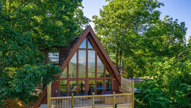 A wooden cabin with a balcony, surrounded by lush greenery. - Views*Close to Dollywood*Keurig*Pool Table*Wifi*Resort Pool (PIGEON FORGE)