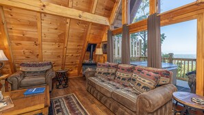 A cozy cabin interior with a wooden ceiling, a sofa with patterned cushions, a small table, and a view of the outdoors. - Views*Close to Dollywood*Keurig*Pool Table*Wifi*Resort Pool (PIGEON FORGE)