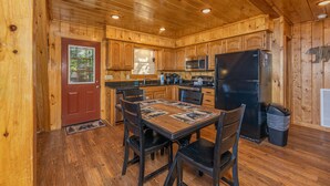A wooden cabin kitchen with a dining table, chairs, a refrigerator, and a microwave. - Views*Close to Dollywood*Keurig*Pool Table*Wifi*Resort Pool (PIGEON FORGE)