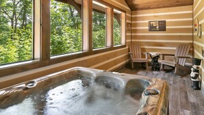 Eine Holzhütte mit Whirlpool, Holzstühlen und Blick auf den Wald durch große Fenster.
