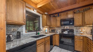 Una cocina con armarios de madera, encimeras de granito, un lavamanos de acero inoxidable, una estufa negra y un microondas.