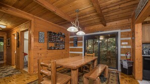 Interior de madera con una mesa de comedor y bancos, techo de madera y vista a través de un ventanal.