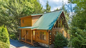 A log cabin with a green metal roof, wooden exterior, and a stone foundation. - Perfect Family Vacation Cabin (GATLINBURG)