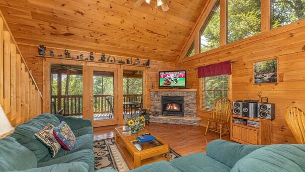 A cozy cabin interior with a stone fireplace, wooden furniture, and large windows. - Perfect Family Vacation Cabin (GATLINBURG)