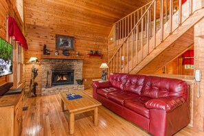 A wooden interior with a stone fireplace, a red leather sofa, and a wooden staircase. - Quaint*Resort Setting*Hot Tub*WiFi*Keurig*Secluded (PIGEON FORGE)