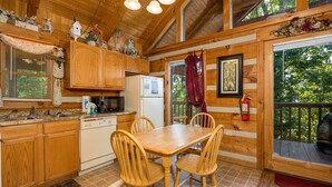 A wooden cabin kitchen with a dining table, chairs, wooden cabinets, a refrigerator, and a window with curtains. - Rustic Studio*Mountain Views*Jacuzzi*Romantic (PIGEON FORGE)
