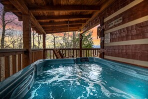 Uma banheira de hidromassagem sob um deck de madeira, com vista para árvores e montanhas.