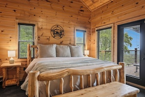 A wooden cabin bedroom with a bed, bedside tables, and a window with a view.