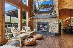 A cozy room with a stone fireplace, comfortable seating, and a large TV mounted on the wall.