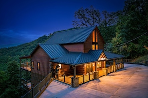 A log cabin with a balcony, a covered porch, and a stone foundation.