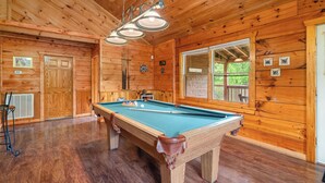 A wooden cabin with a pool table, wooden walls, and a large window. - Luxury Log Home*Views*Close to Pigeon Forge*WiFi*Hot Tub (PIGEON FORGE)