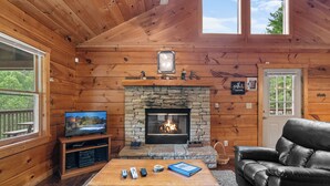 A cozy cabin interior with a stone fireplace, wooden walls, a television, and a leather sofa. - Luxury Log Home*Views*Close to Pigeon Forge*WiFi*Hot Tub (PIGEON FORGE)