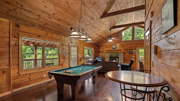A wooden cabin interior with a pool table, a fireplace, and large windows offering views of the outdoors. - Luxury Log Home*Views*Close to Pigeon Forge*WiFi*Hot Tub (PIGEON FORGE)