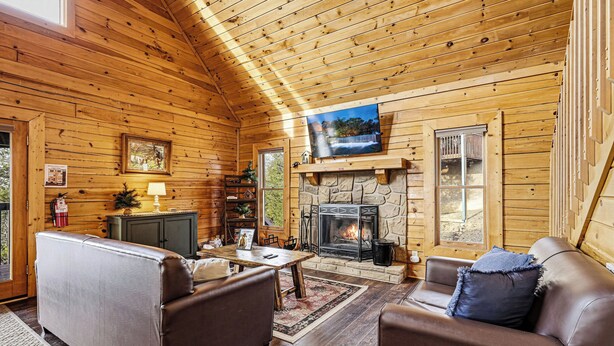 Interior acogedor de una cabaña con chimenea de piedra, paredes de madera, un televisor y repisa de la chimenea.