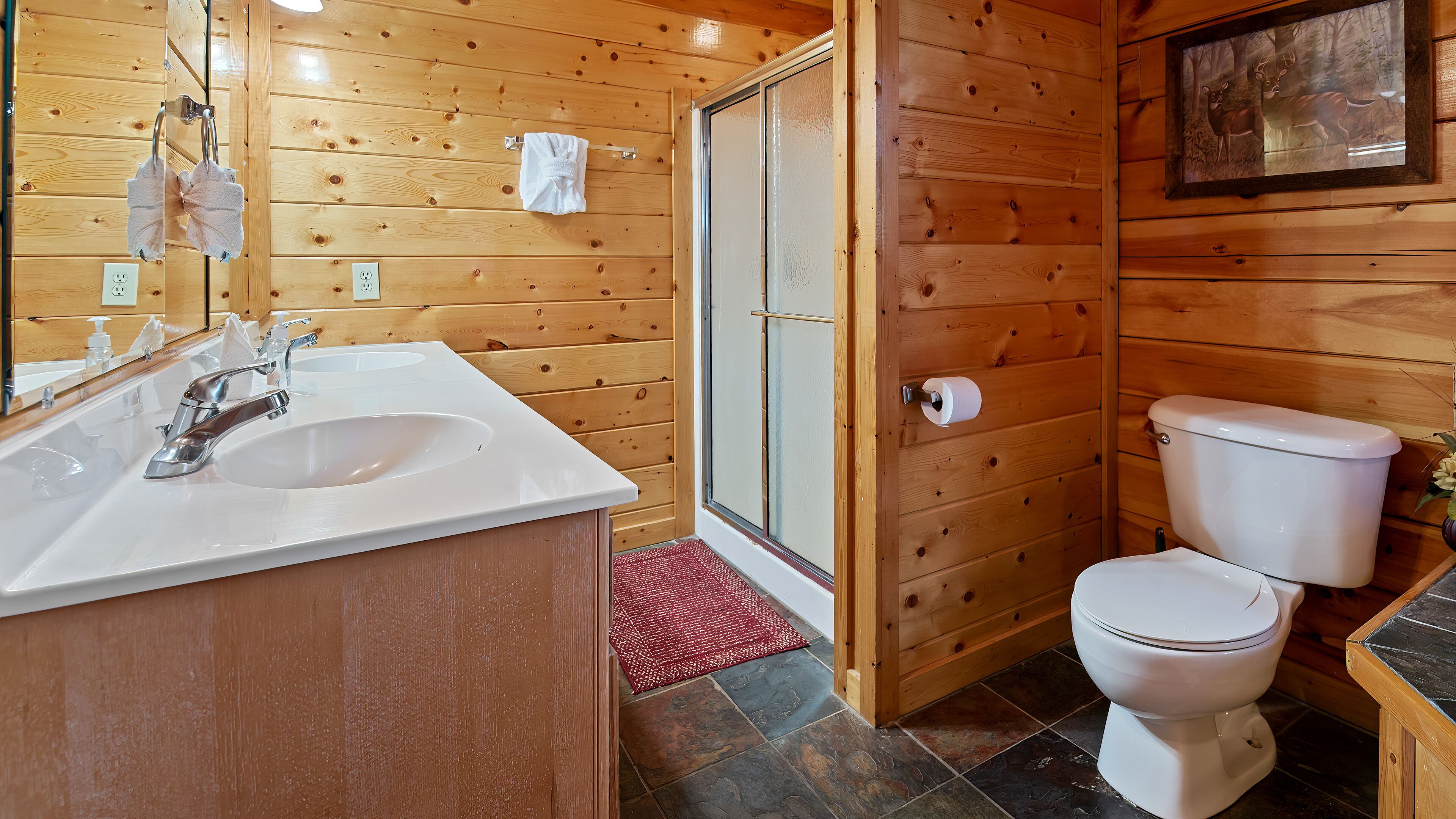 A wooden interior bathroom with a sink, toilet, and glass shower door.