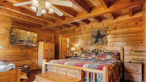 Interior de uma cabana de madeira com uma cama, armários de madeira, um ventilador de teto e uma pintura de uma cabana no outono.
