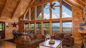 Eine geräumige Blockhütte mit großen Fenstern, einem Essbereich und einem gemütlichen Wohnzimmer mit zwei Sofas und einem Couchtisch.