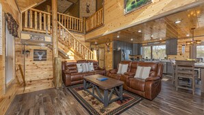 A spacious living area with a wooden staircase, leather sofas, and a kitchen in the background. - Cabin with Indoor Pool and Lots of Entertainment (PIGEON FORGE)