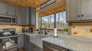 A modern kitchen with granite countertops, stainless steel appliances, and a large window overlooking a deck. - Cabin with Indoor Pool and Lots of Entertainment (PIGEON FORGE)