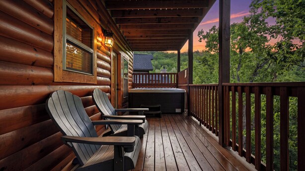 A wooden cabin with a porch, Adirondack chairs, and a hot tub. - Cabin with Indoor Pool and Lots of Entertainment (PIGEON FORGE)