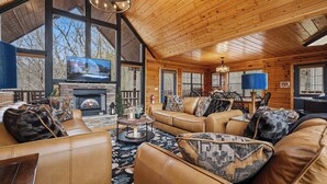 A cozy log cabin interior with leather sofas, a fireplace, a television, and large windows. - 4-Bedroom Cabin near Dollywood (SEVIERVILLE)