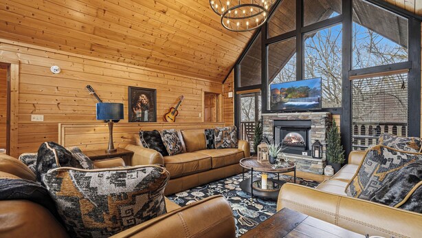 A cozy log cabin interior with a fireplace, leather furniture, and large windows. - 4-Bedroom Cabin near Dollywood (SEVIERVILLE)