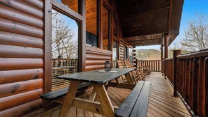A wooden deck with picnic tables and benches, large windows, and a view of the surrounding landscape. - 4-Bedroom Cabin near Dollywood (SEVIERVILLE)