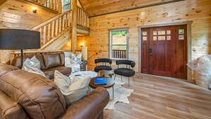 Un intérieur en bois avec un escalier, un canapé en cuir, des fauteuils et une porte.