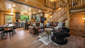 Un intérieur de cabine spacieux, avec un escalier en bois, un coin repas, un salon doté d’un canapé et d’une table basse, et une cuisine équipée d’appareils modernes.